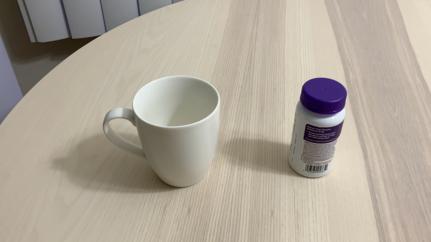 A photo of a white mug and a purple-capped bottle on a round wooden table, the first of two near-identical frames.