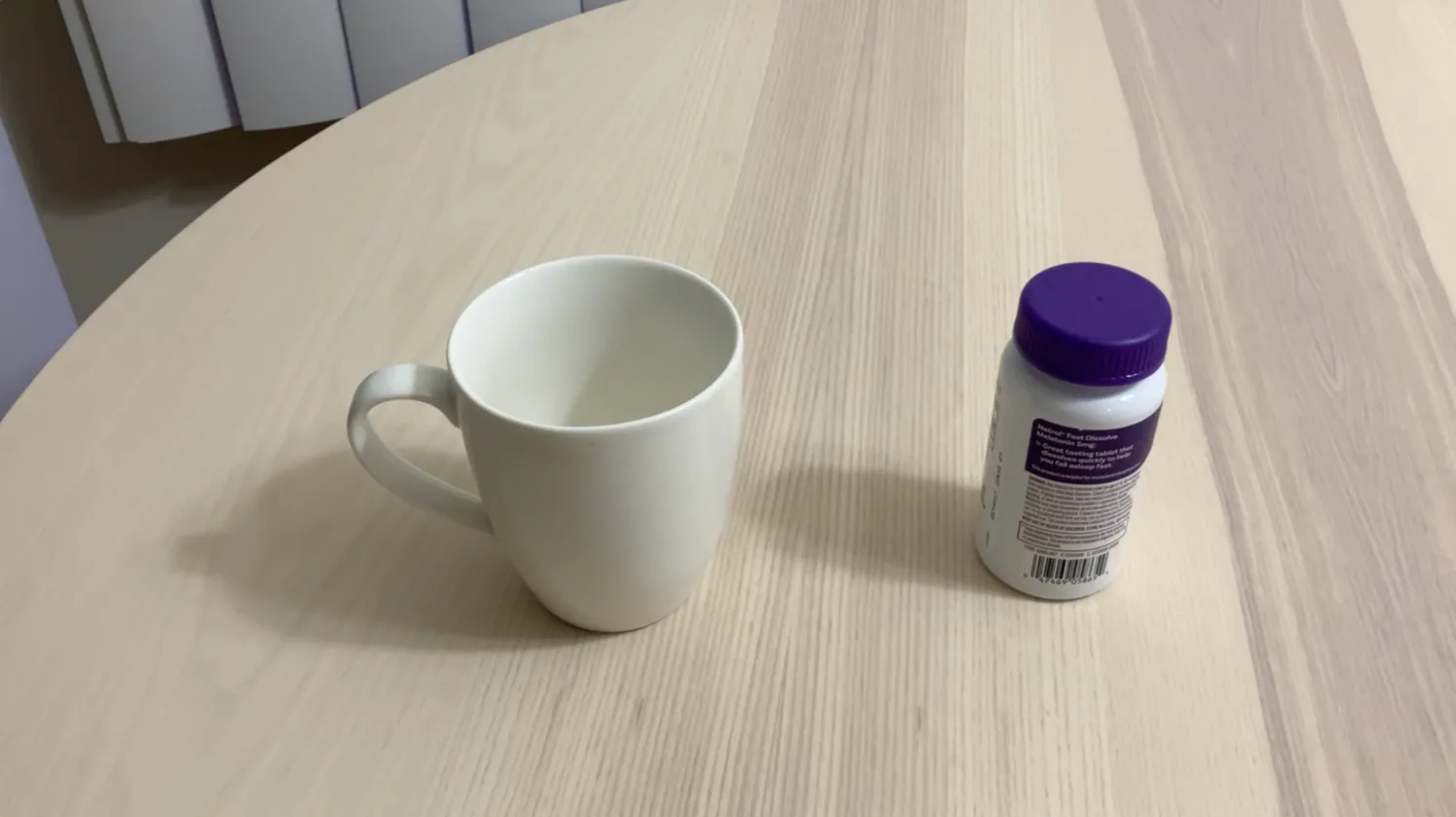 A photo of a white mug and a purple-capped bottle on a round wooden table, the first of two near-identical frames.